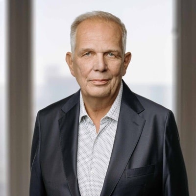Professionele portretfoto van een oudere man in een donkere blazer en een licht overhemd, die in de camera kijkt.